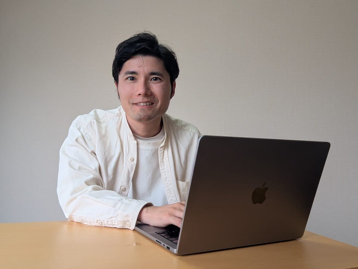白壁の前でノートPCを開いている津留将史
